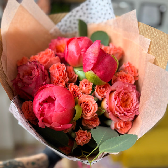 Bouquet of pink and orange flowers wrapped in brown paper held by a person.