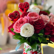 Bouquet of red, pink, and white flowers in a floral-patterned vase on a table.