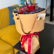 Bouquet of flowers wrapped in brown paper with a red ribbon on a table.