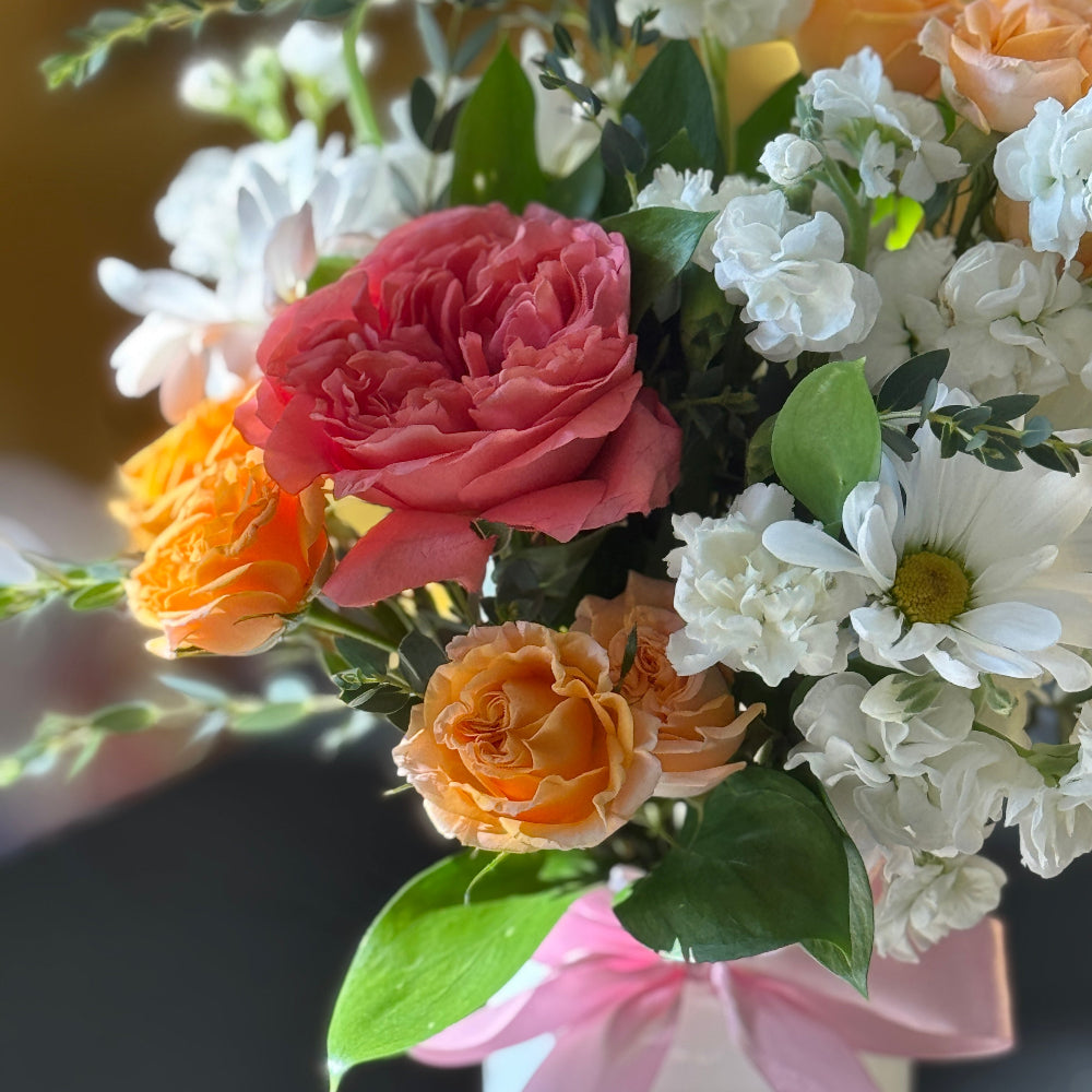Bouquet of flowers with pink, orange, and white flowers tied with a pink ribbon on a blurred background.