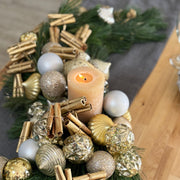 Close-up of pine holiday centerpiece with gold-painted cinnamon sticks and metallic ornaments