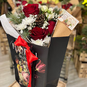 Bouquet of red roses and white flowers in a black box with a red ribbon, set against a blurred floral shop background.