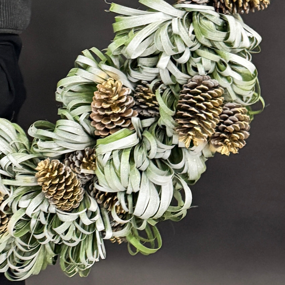 Close-up of snowy palm leaves and golden pinecones on handcrafted holiday wreath.