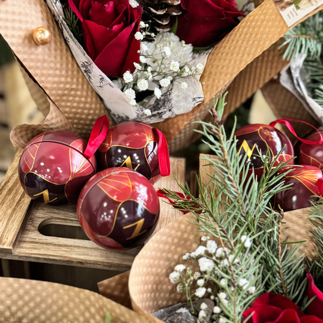 Decorative arrangement with red roses, pinecones, and Christmas ornaments on a wooden surface.