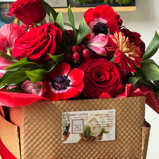 Elegant red roses and anemones arranged with hypericum berries and seasonal blooms in a beautiful pink ceramic vase packed in beautiful box