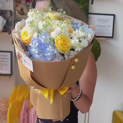 Romantic spring and summer bouquet featuring yellow roses, blue hydrangea.
