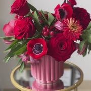 Sophisticated red rose and anemone arrangement in a pink clay vase, handcrafted by Flowers’ Cuddles in Springfield, VA.