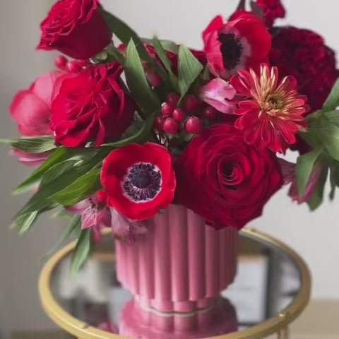 Sophisticated red rose and anemone arrangement in a pink clay vase, handcrafted by Flowers’ Cuddles in Springfield, VA.