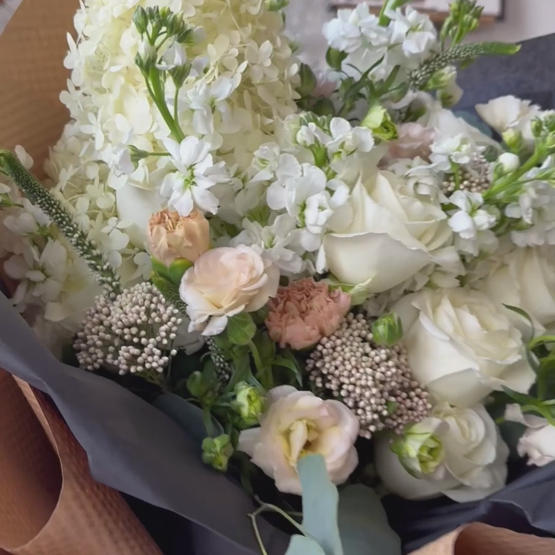 Video of gorgeous bouquet of white and cream flowers, wrapped in black tissue with black ribbon and black accessories and Kraft paper 