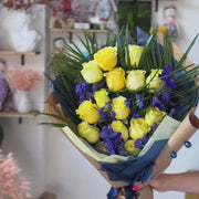Playful graduation flower arrangement in yellow and blue with tropical palm accents