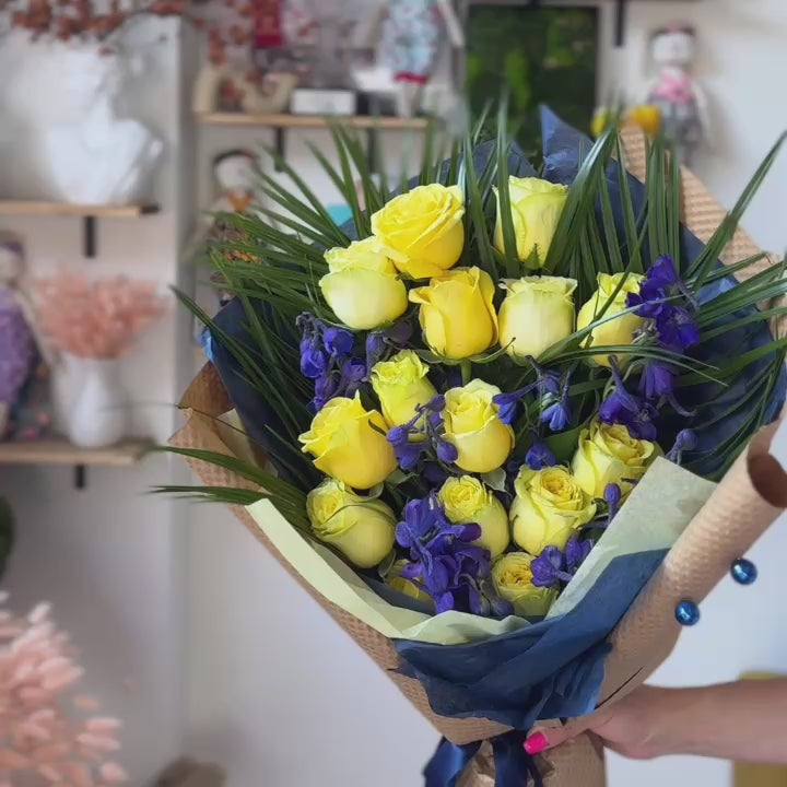 Playful graduation flower arrangement in yellow and blue with tropical palm accents