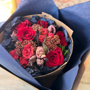 Bouquet of red roses and brown tulips wrapped in blue paper in the box.