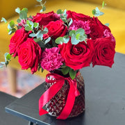 Bouquet of red roses and pink flowers in a decorative vase on a table.