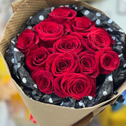 Bouquet of red roses wrapped in brown paper with black and white polka dot ribbon.
