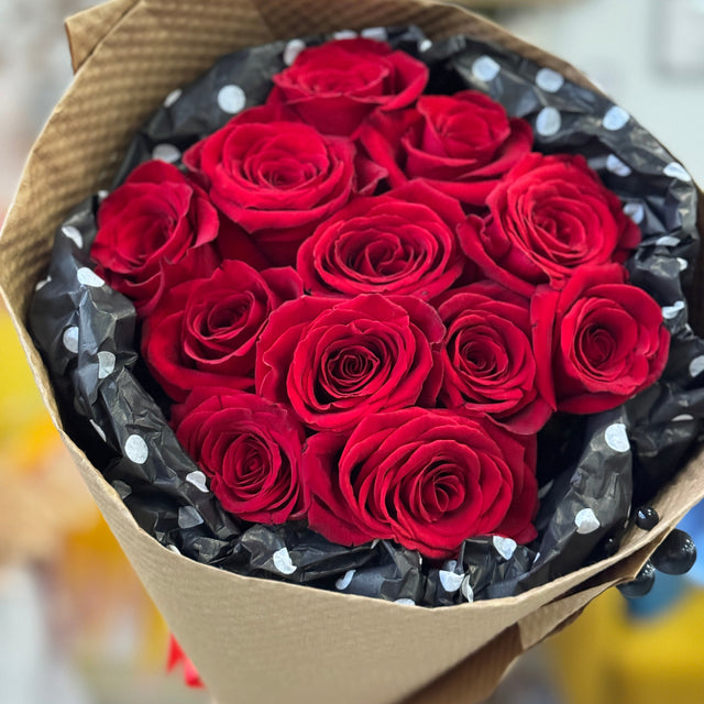 Bouquet of red roses wrapped in brown paper with black and white polka dot ribbon.