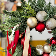 Decorative Christmas arrangement with greenery, red and gold ornaments, and ribbons.