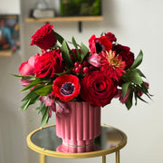 Designer floral centerpiece with rich red blooms, textured hypericum berries, and elegant seasonal flowers in a pink vase.