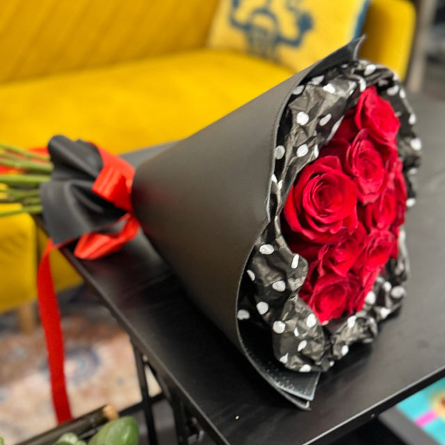 Bouquet of red roses in a black wrap with polka dots on a yellow couch.