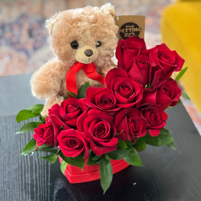 Bouquet of red roses with a teddy bear and a red bow on a textured surface.