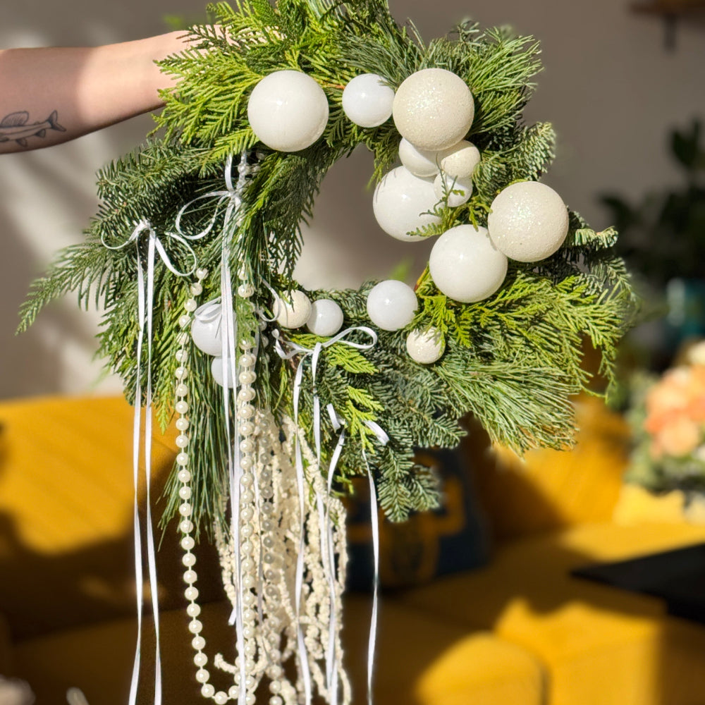 Decorative wreath with white ornaments and greenery on a yellow surface