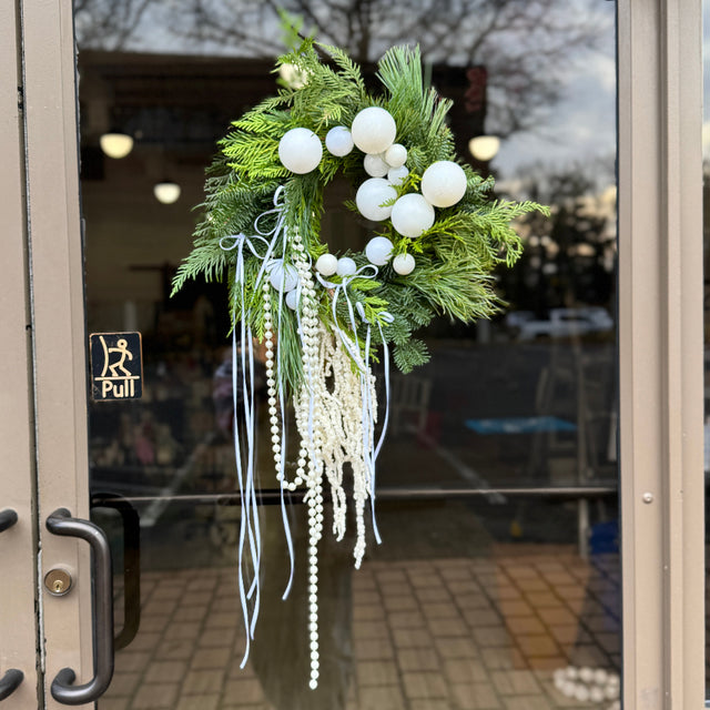 Decorative wreath with white ornaments and greenery on a glass door.